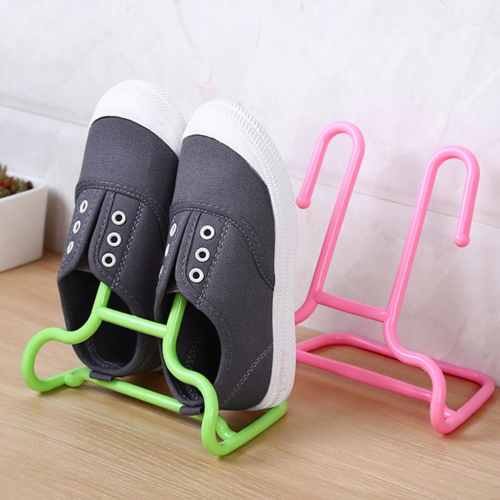 A pair of grey canvas shoes hangs from a green plastic shoe drying rack, with a pink rack standing nearby on a wooden